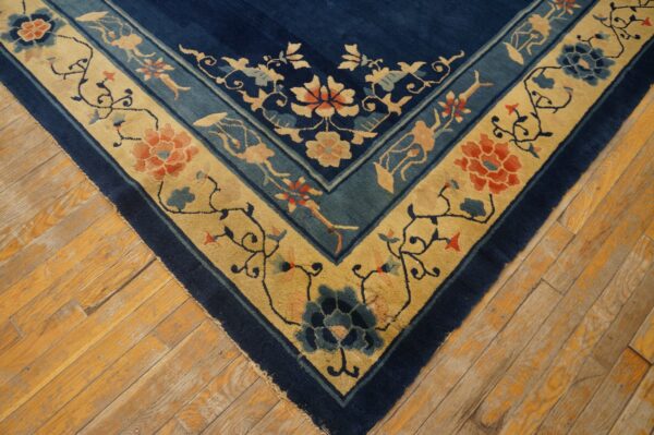 Navy blue rug featuring elaborate gold and teal borders with detailed floral and vine patterns on wood planks.