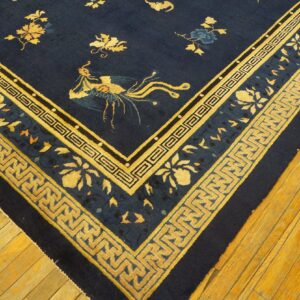 A navy blue rug featuring gold floral and phoenix patterns with key borders rests on warm plank wood flooring.