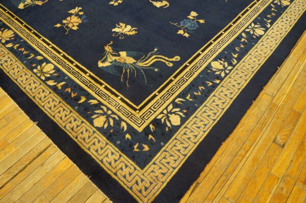A navy blue rug featuring gold floral and phoenix patterns with key borders rests on warm plank wood flooring.