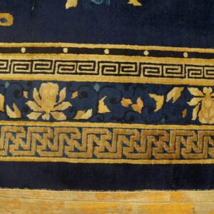 Navy blue rug border with stacked golden floral and two geometric key patterns on worn wood flooring.