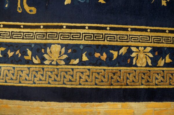 Navy blue rug border with stacked golden floral and two geometric key patterns on worn wood flooring.