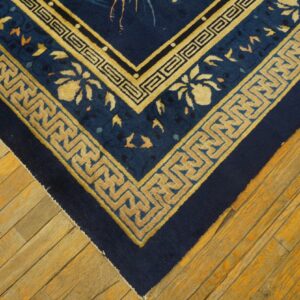 Navy blue rug corner with gold meander borders rests on rustic light brown wooden planks.