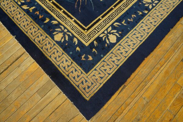 Navy blue rug corner with gold meander borders rests on rustic light brown wooden planks.