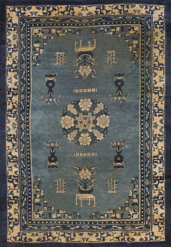 Muted blue low-pile rug featuring an elaborate beige and navy medallion, vases, and ornate border designs.