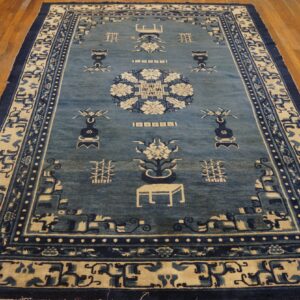 Blue and cream rug with traditional Asian symbols and borders, set on wide plank wood flooring.