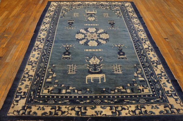 Blue and cream rug with traditional asian symbols and borders, set on wide plank wood flooring.