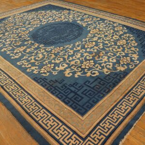 Blue and tan ornate rug with floral motifs and geometric borders resting on light wood flooring.