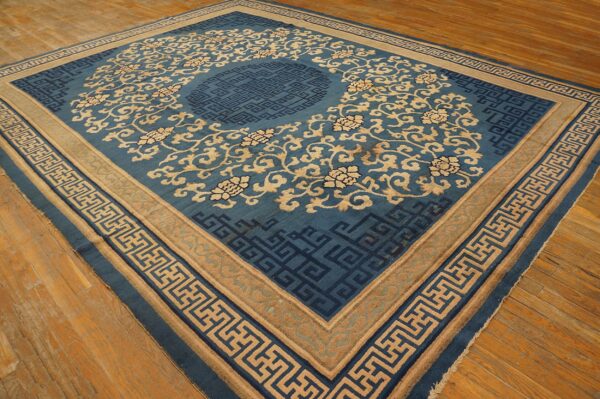 Blue and tan ornate rug with floral motifs and geometric borders resting on light wood flooring.