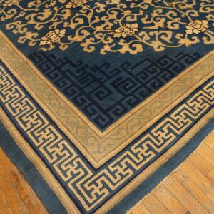 Close-up of a blue rug with tan floral field and geometric borders on natural wood plank flooring.