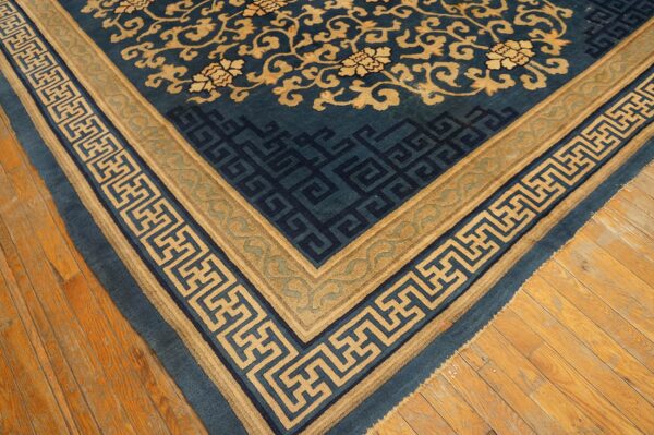 Close-up of a blue rug with tan floral field and geometric borders on natural wood plank flooring.