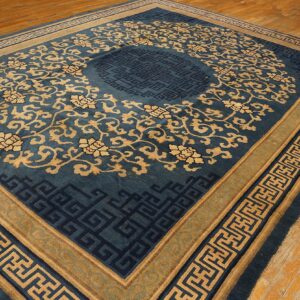 Teal blue rug with tan floral motifs and dark geometric fretwork borders over distressed wood floors.