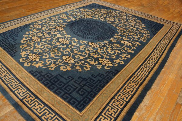 Teal blue rug with tan floral motifs and dark geometric fretwork borders over distressed wood floors.