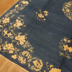 Deep blue rug with an ornate beige and sage green floral pattern on light brown hardwood planks.