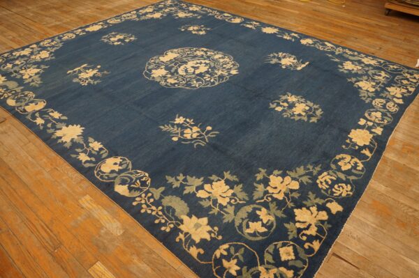 Square blue rug featuring large yellow and pale blue floral motifs on exposed wood planks.