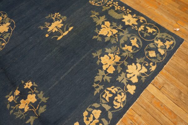 A dark blue rug with gold and green floral borders lies on aged light brown wood planks.