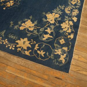 Detail of a deep blue floral rug with yellow and green designs on light brown hardwood planks.