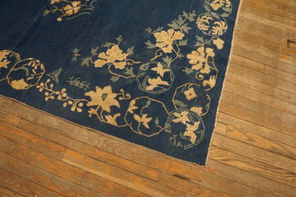 Detail of a deep blue floral rug with yellow and green designs on light brown hardwood planks.