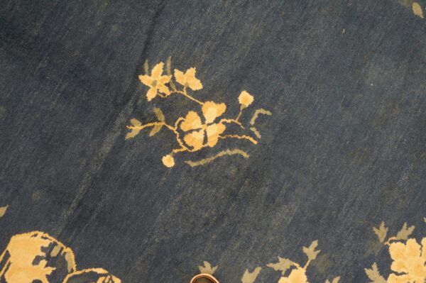 Dark navy rug with a visible low pile texture featuring stylized floral motifs in gold and pale green.