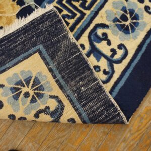 A navy, light blue, and tan floral rug is folded back, revealing its reverse weave structure on wood flooring.
