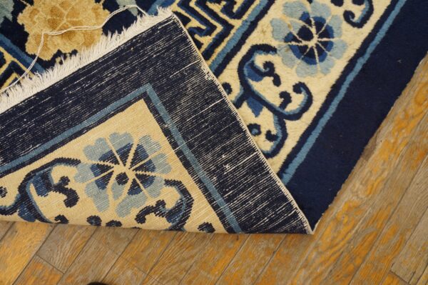 A navy, light blue, and tan floral rug is folded back, revealing its reverse weave structure on wood flooring.