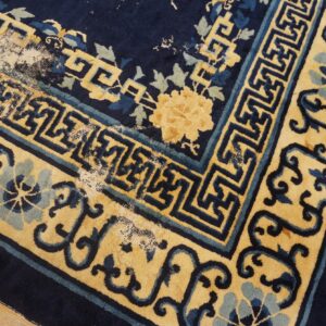 Low-pile navy and yellow rug corner showing geometric borders, floral patterns, and significant pile loss on wood.