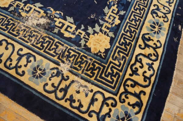 Low-pile navy and yellow rug corner showing geometric borders, floral patterns, and significant pile loss on wood.