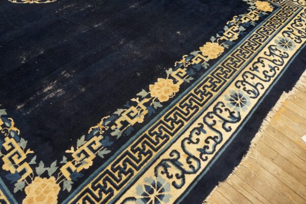 Dark blue rug corner shows gold and blue floral and geometric borders resting on light wood plank flooring.