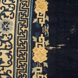 Dark blue rug detail shows cream, light blue, and gold floral borders, with visible wear spots.