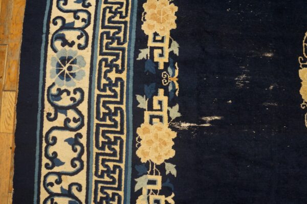 Dark blue rug detail shows cream, light blue, and gold floral borders, with visible wear spots.