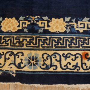 Thick-pile navy and cream rug border shows scrolling florals and geometric motifs over wooden flooring.