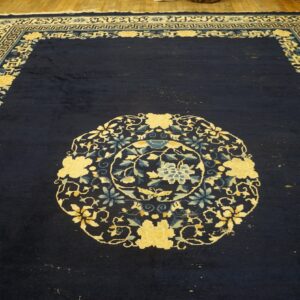 Dark blue rug with a central floral medallion and yellow and light blue patterned borders on a wood floor.