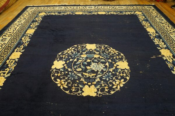 Dark blue rug with a central floral medallion and yellow and light blue patterned borders on a wood floor.