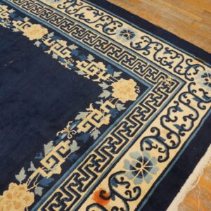 Navy blue rug corner with thick cream and blue floral and geometric borders rests on wood floor.