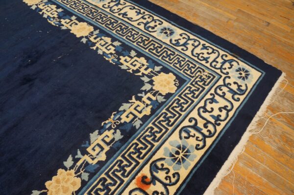 Navy blue rug corner with thick cream and blue floral and geometric borders rests on wood floor.