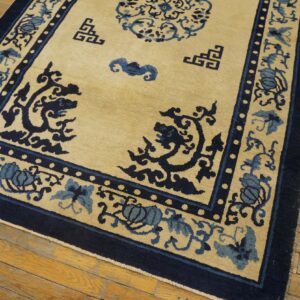 Tan rug with deep navy and light blue elaborate patterns rests on worn hardwood planks.