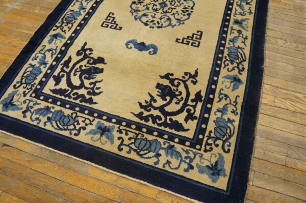 Tan rug with deep navy and light blue elaborate patterns rests on worn hardwood planks.