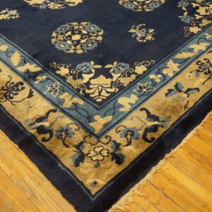 Navy blue floral rug with gold and teal borders rests on highly polished hardwood flooring.