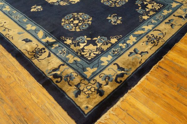 Navy blue floral rug with gold and teal borders rests on highly polished hardwood flooring.