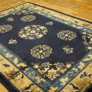 Navy blue and gold rug featuring ornate floral medallions and borders laid on wood flooring.