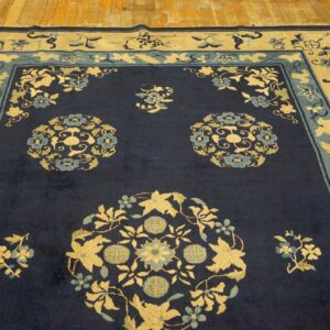Navy rug with dense gold and teal floral medallions and multi-layered borders on light wood flooring.