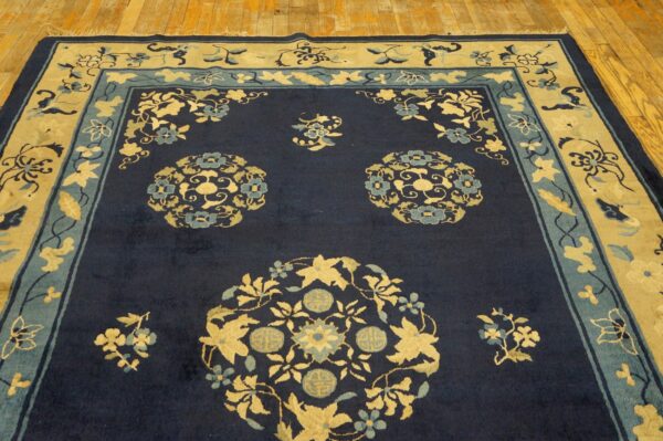 Navy rug with dense gold and teal floral medallions and multi-layered borders on light wood flooring.
