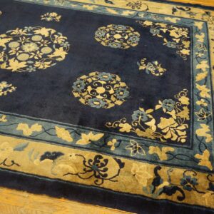 Navy blue rug features gold and teal floral medallions and multi-layered borders on light hardwood flooring.