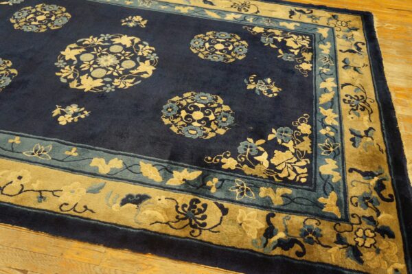 Navy blue rug features gold and teal floral medallions and multi-layered borders on light hardwood flooring.