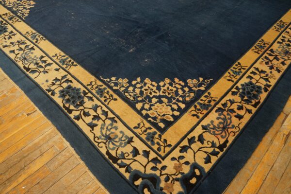 Blue rug corner with a tan floral border on worn, wide-plank wooden flooring.