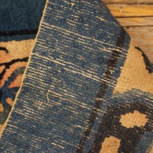 Blue and tan patterned rug folded to show its woven reverse texture resting on distressed wood planks.
