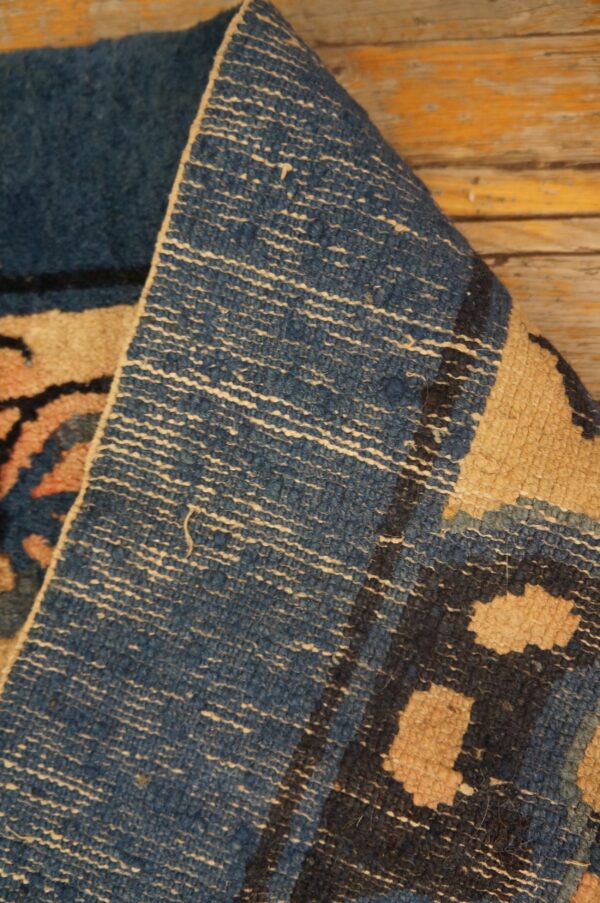 Blue and tan patterned rug folded to show its woven reverse texture resting on distressed wood planks.