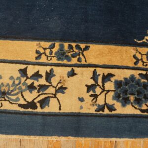 Navy blue rug border and golden bands with intricate blue and tan floral designs on wooden planks.