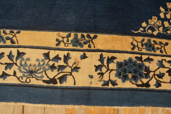 Navy blue rug border and golden bands with intricate blue and tan floral designs on wooden planks.