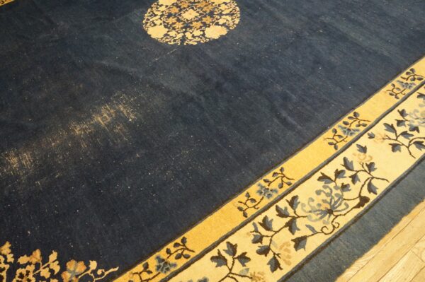 Navy blue rug detail with cream and yellow floral borders resting on a light hardwood floor.