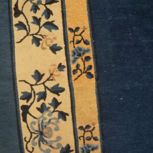 Navy blue rug field bordered by a wide beige panel with blue flowers on light wood flooring.